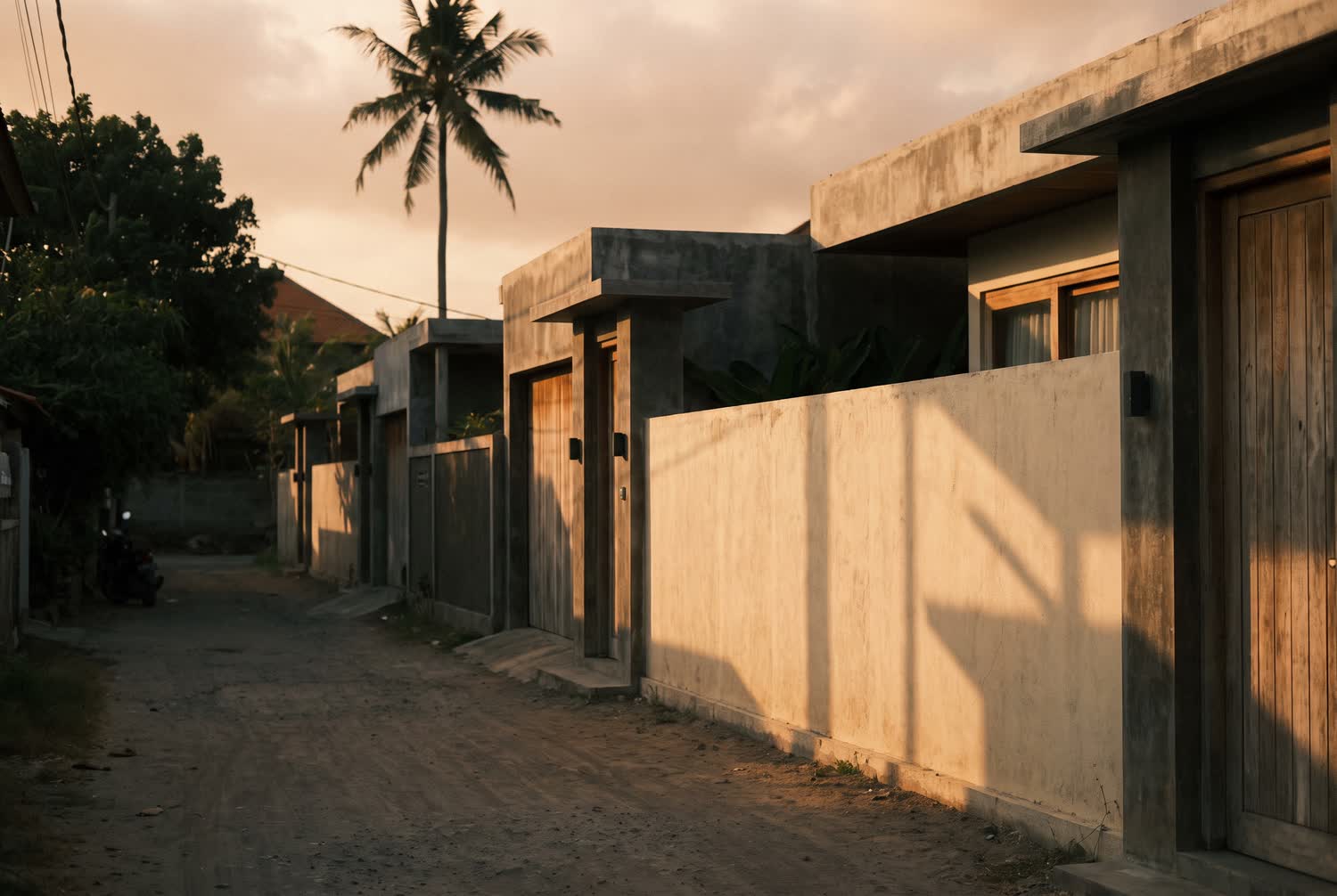 A contemporary coastal street in Canggu with low concrete and timber architecture and evening light on the wall.