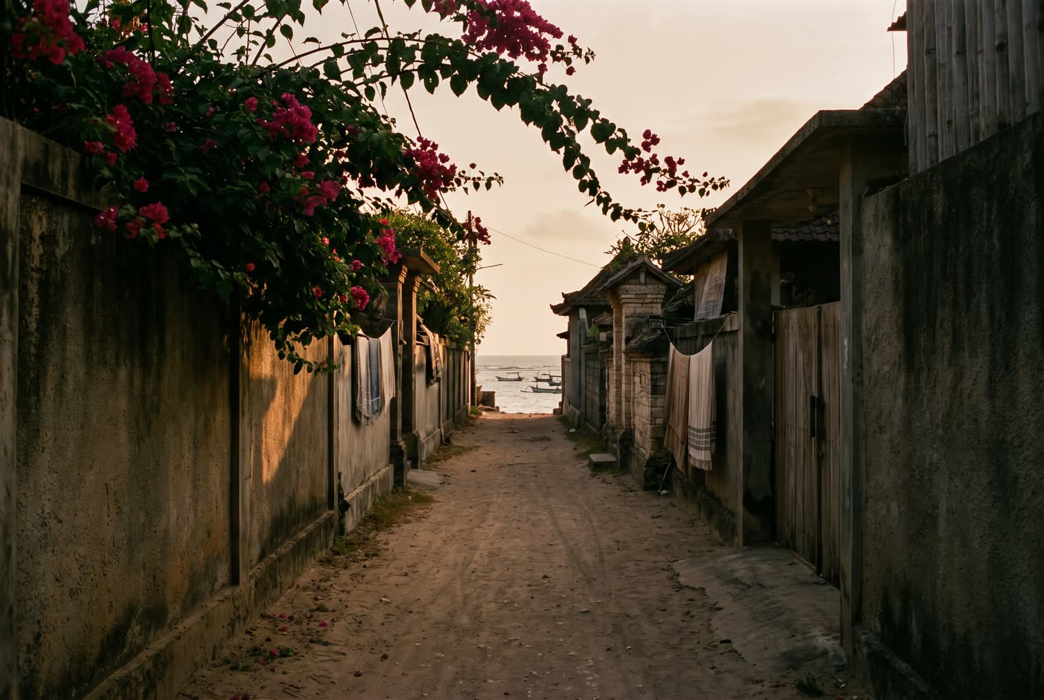 A warm coastal lane in Jimbaran with weathered concrete, bougainvillea and the sea glimpsed at the end of the lane.